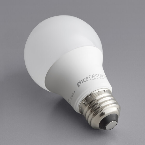 A TCP Pro Line frosted LED light bulb on a gray surface.