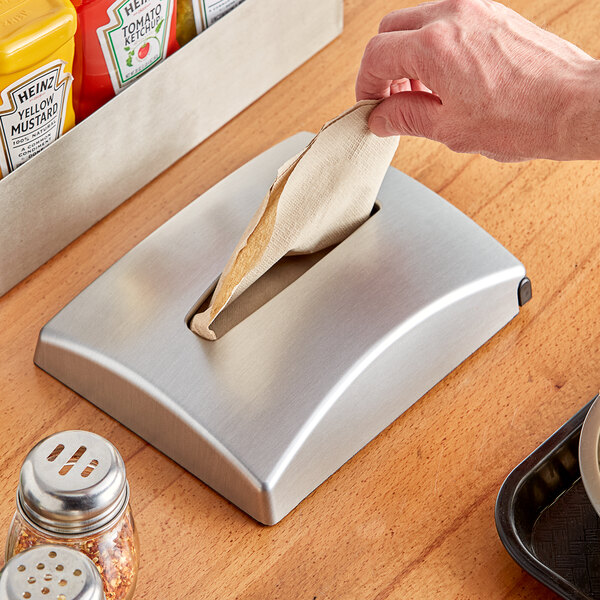 A hand putting a napkin in a Dixie Ultra in-counter napkin dispenser with a stainless faceplate.
