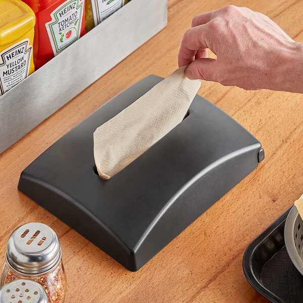 A hand putting a napkin in a Dixie Ultra In-Counter Interfold Napkin Dispenser on a counter.
