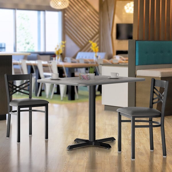 A Lancaster Table & Seating table top and base with chairs and a cup on a table in a restaurant.