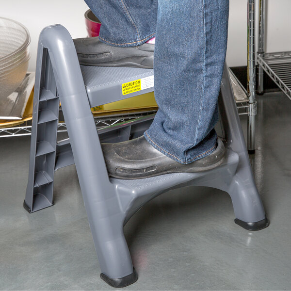 A person's feet on a Rubbermaid two-step step stool.