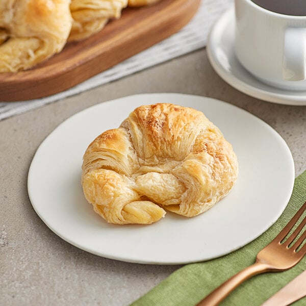 A plate with a Premium Curved Butter Croissant and a cup of coffee.