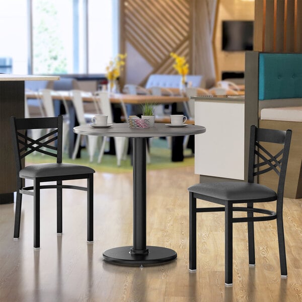 A Lancaster Table & Seating table with a white and gray surface and a black base with two black chairs at it.