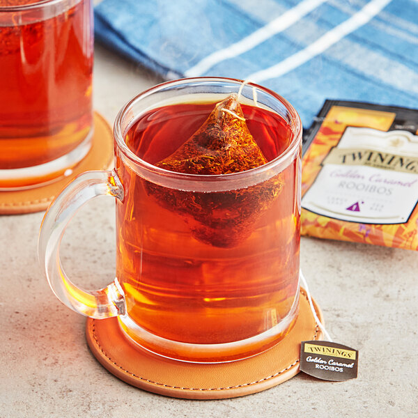 A glass mug of Twinings Golden Caramel Rooibos tea with a tea bag in it.