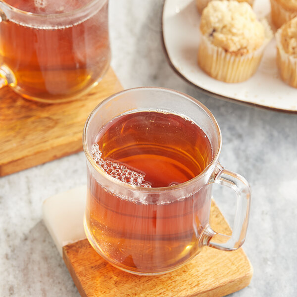 A glass mug of Twinings Earl Grey tea on a wooden coaster with a plate of muffins.