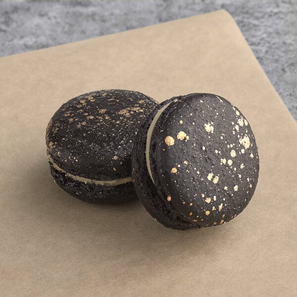 Two black Macaron Centrale Luxe macarons with gold specks on top.