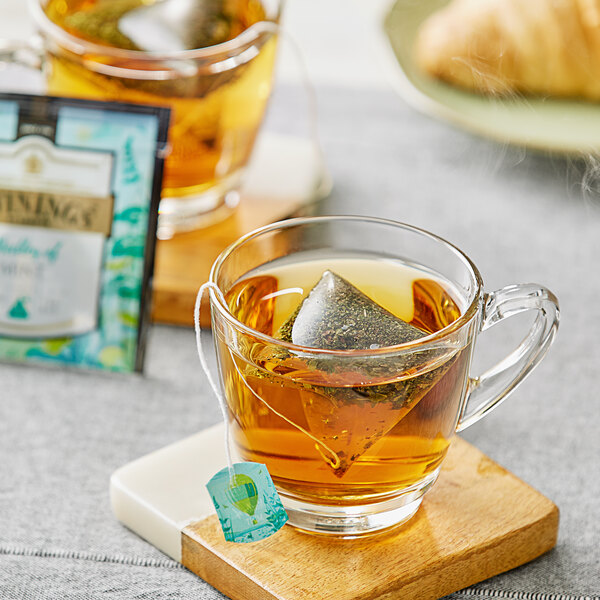 A glass cup of Twinings mint tea with a pyramid tea bag in it.
