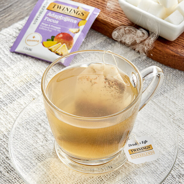 A glass mug of Twinings Focus Ginseng, Mango & Pineapple herbal tea with a tea bag in it.