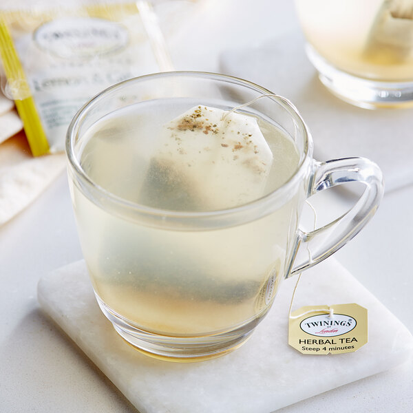 A glass mug of Twinings Lemon & Ginger herbal tea with a tea bag in it.