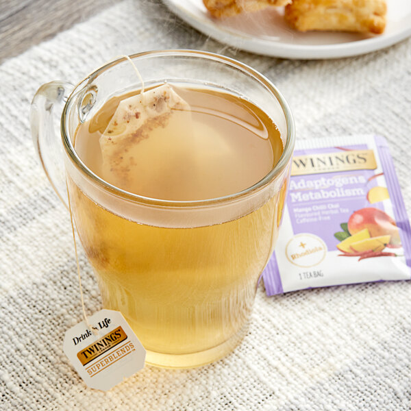 A glass cup of Twinings Boost Adaptogens Mango Chili Chai Tea with a tea bag in it.
