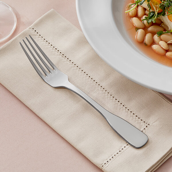 An Acopa Triumph stainless steel table fork on a napkin next to a plate of food.