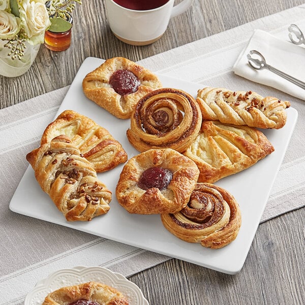 A plate of Schulstad large assorted Danish pastries on a table with a white cup of coffee.