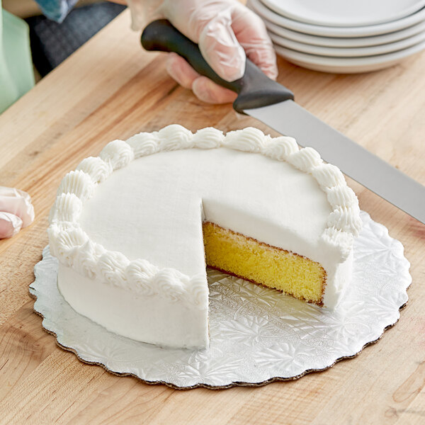 A person cutting a cake on a Enjay silver corrugated cake circle with a knife.