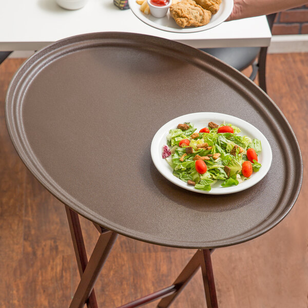 A Carlisle Griptite 2 oval non skid fiberglass serving tray holding a plate of salad with tomatoes and lettuce.