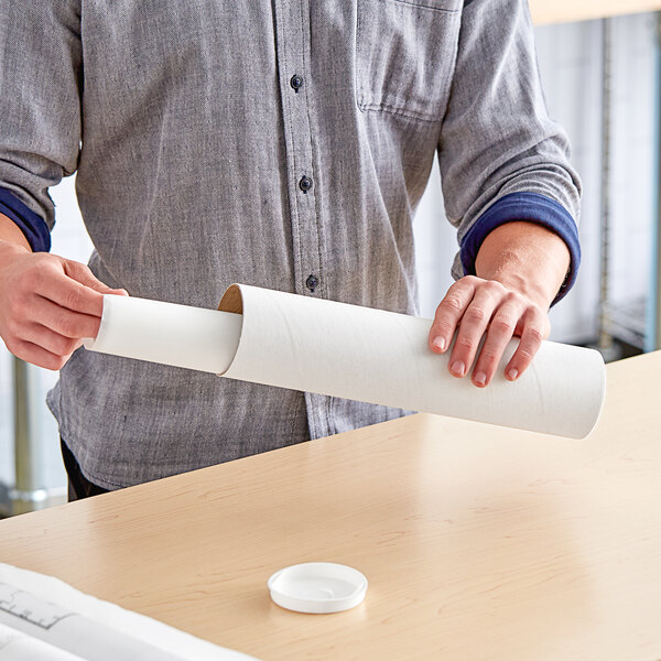 A person holding a Lavex white mailing tube filled with paper on a table.