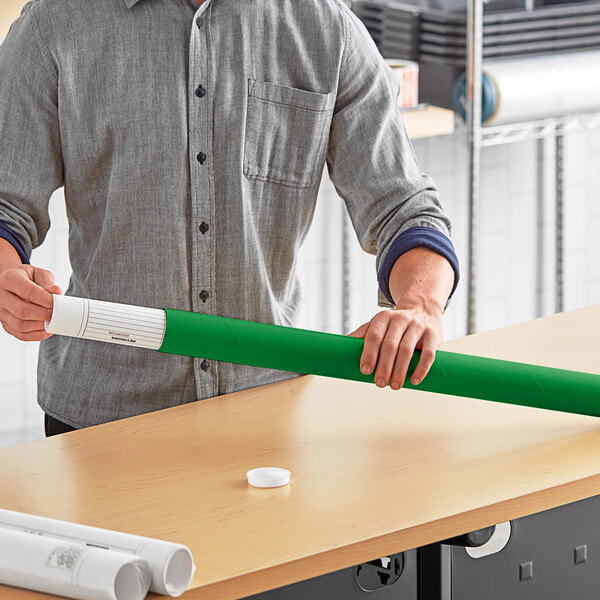 A man holding a green Lavex mailing tube with a rolled up white paper inside.