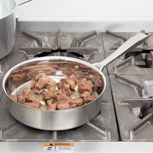 A Vollrath Intrigue saute pan with meat cooking on a stove.