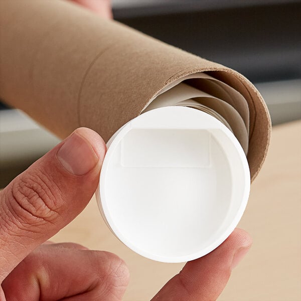 A hand holding a white plastic lid over a white mailing tube.