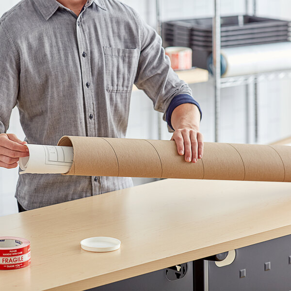 A person holding a Lavex Kraft mailing tube filled with brown paper.