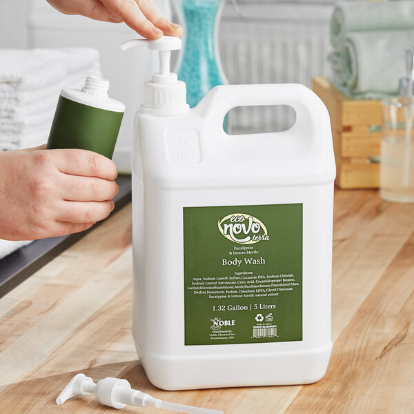 A person using a pump dispenser to pour Noble Eco Novo Terra body wash from a white and green plastic bottle.