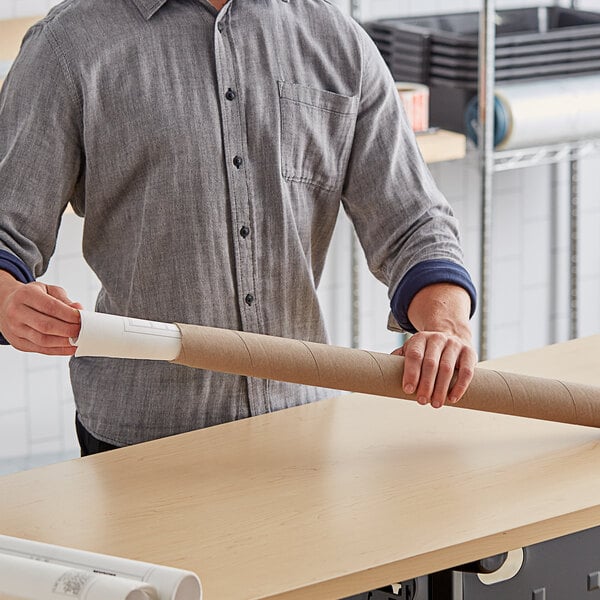 A man holding a long Lavex Kraft cardboard tube on a table.
