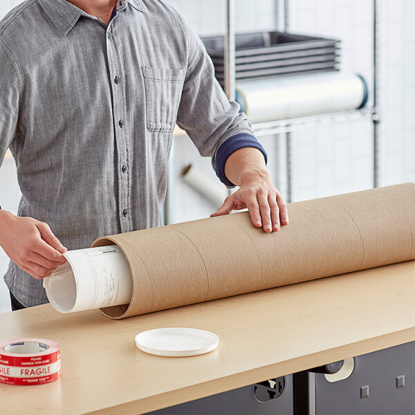 A man using a Lavex heavy-duty mailing tube to hold a roll of brown paper.