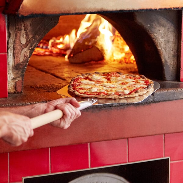 A person using an American Metalcraft aluminum pizza peel to put a pizza in a stone oven.