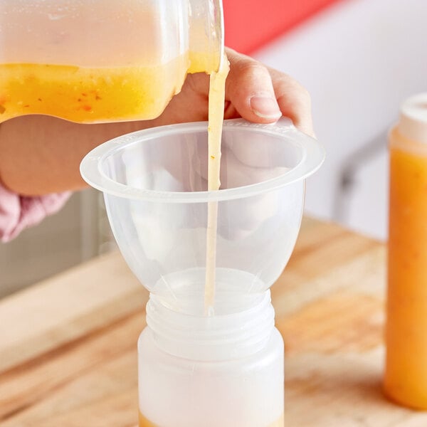 A person using a Choice plastic funnel to pour yellow liquid into a squeeze bottle.