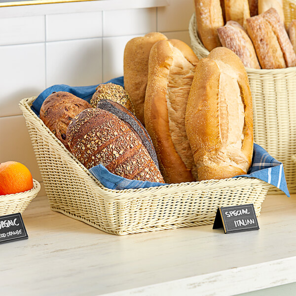 An Acopa woven plastic rattan basket of bread on a bakery display counter.