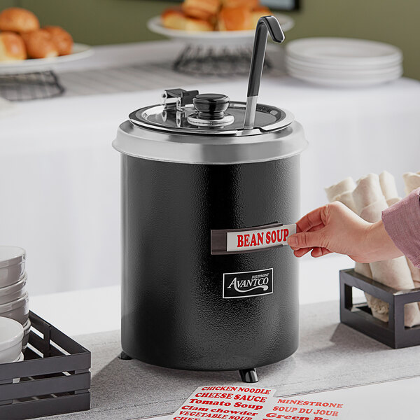 A hand holding a card in a black soup warmer.