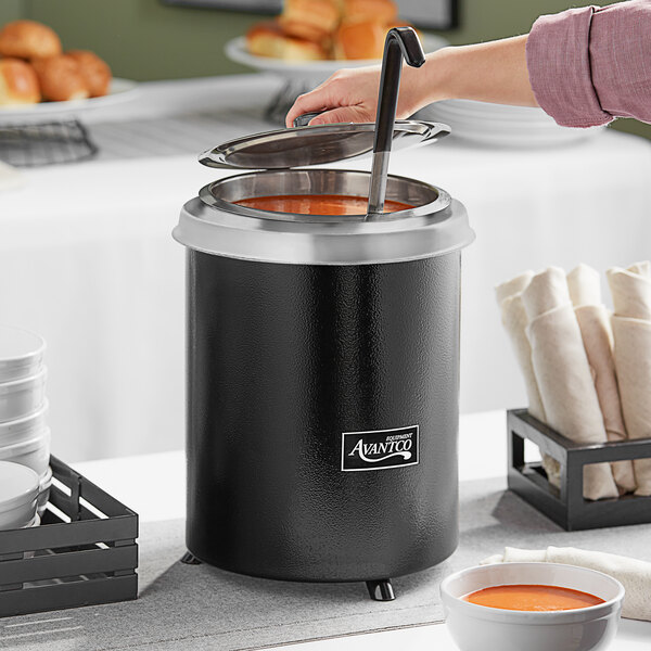 A person using a black Avantco soup warmer to ladle soup into a bowl.