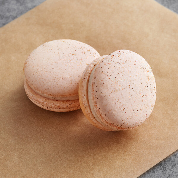 Two Macaron Centrale cinnamon butterscotch macarons on a white paper.