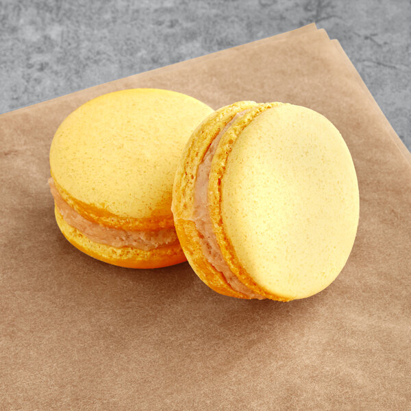 Two yellow Macaron Centrale macarons on a brown surface.