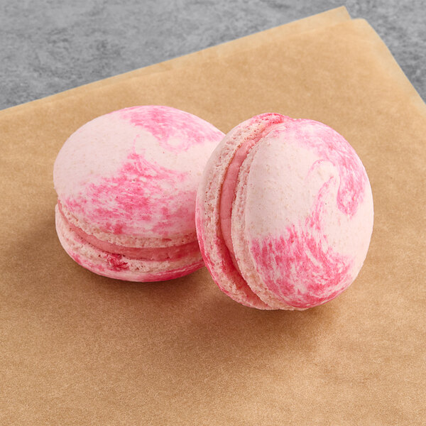 Two pink and white dragon fruit macarons on a brown surface.