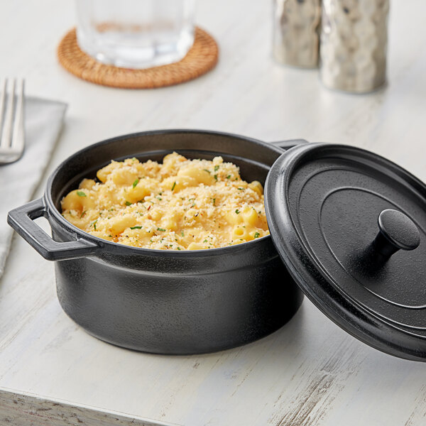 An Elite Global Solutions black faux cast iron melamine pot with a lid on a table with a pot of macaroni and cheese.