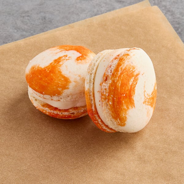 Two orange and white Macaron Centrale cookies on a brown surface.