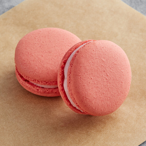 Two Macaron Centrale cherry pecan macarons with pink shells on a brown surface.