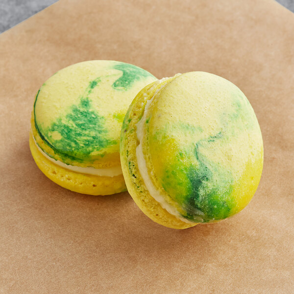 Two yellow and green Macaron Centrale Kaffir Lime macarons on a brown surface.