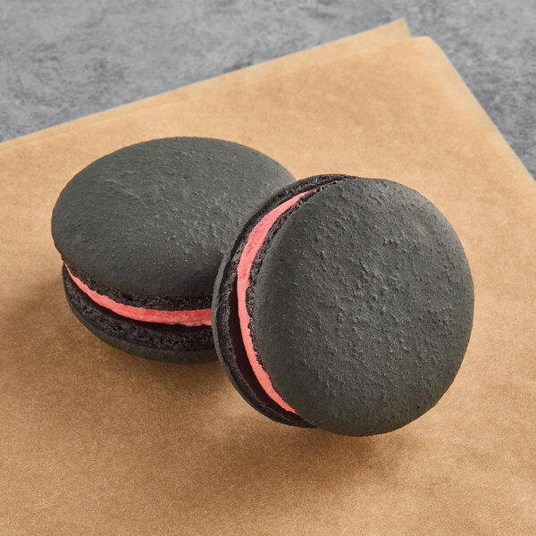 Two black Macaron Centrale macarons with pink filling on a brown paper.