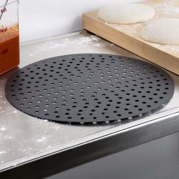 A pizza on an American Metalcraft hard coat anodized aluminum perforated pizza disk.