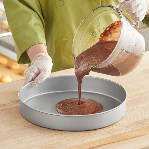 A woman pouring brown liquid into a Baker's Mark round cake pan.