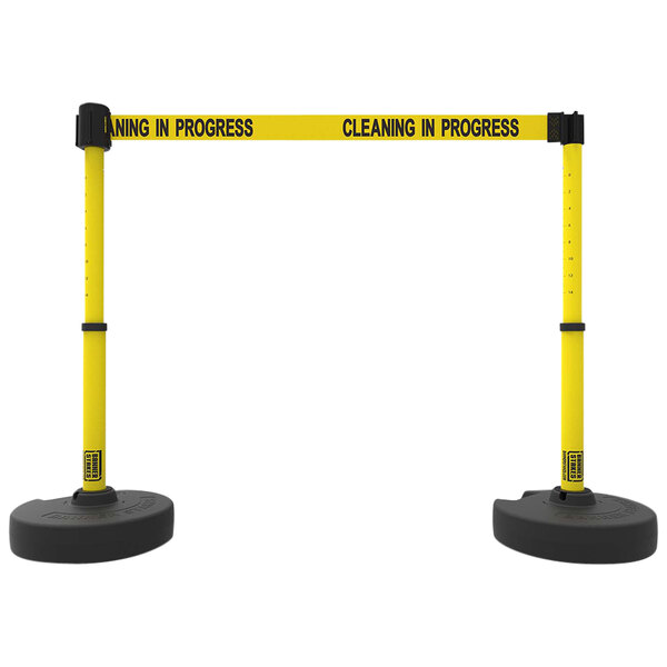 Two yellow and black Banner Stakes retractable barriers with a sign that says "Cleaning in Progress" in white.