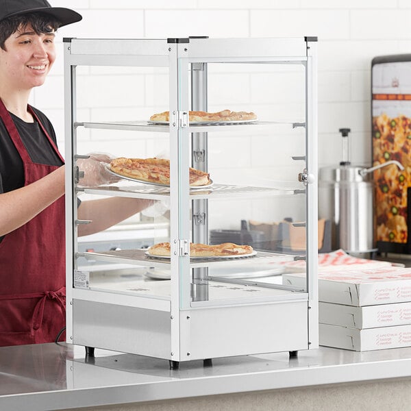 A woman in a red apron using a Carnival King countertop warmer to display pizzas.