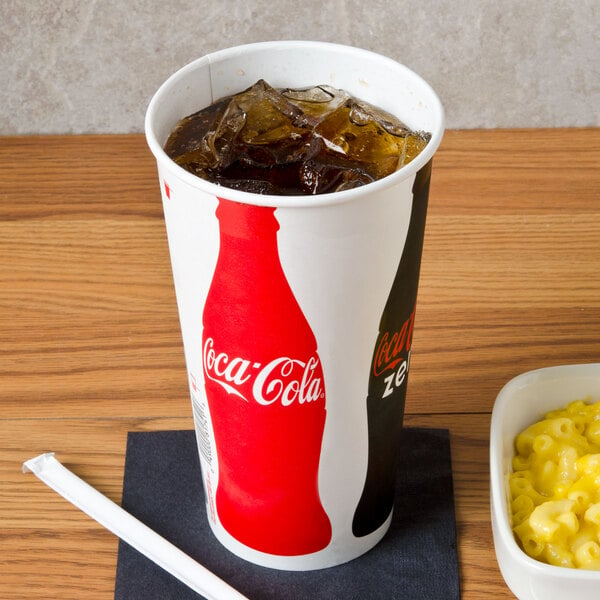 A Solo Coke poly paper cold cup filled with soda and ice on a table with macaroni and cheese.