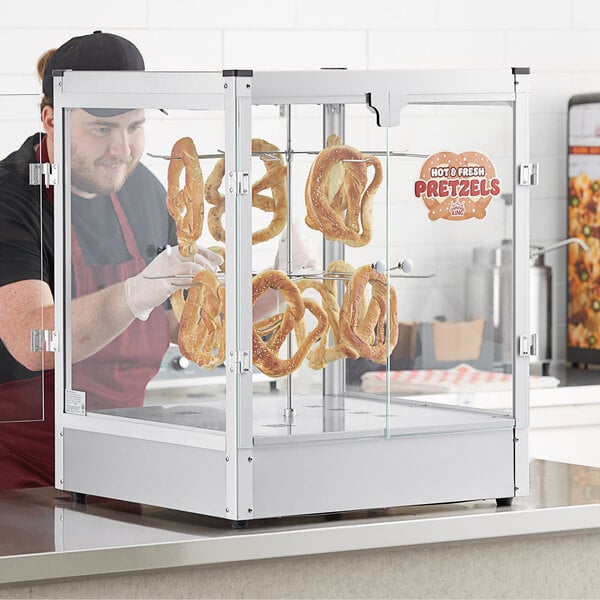 A man in a black shirt and apron using a Carnival King countertop pretzel display case to hold pretzels.
