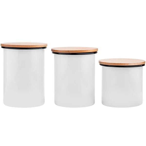 A group of white Tablecraft enamelware canisters with wooden lids.
