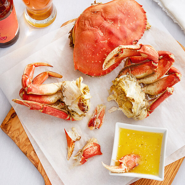 A Dungeness crab on a paper towel with a crab claw in a bowl of sauce.