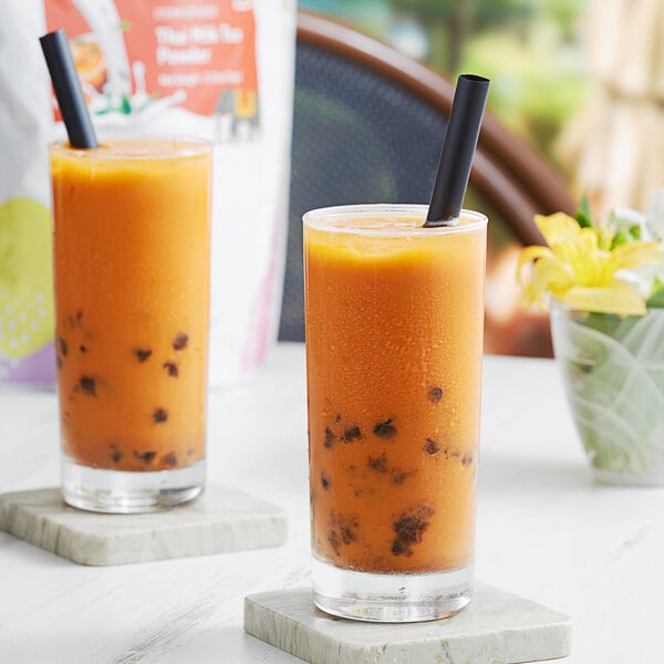 Two glasses of Bossen Thai tea with straws on a table.