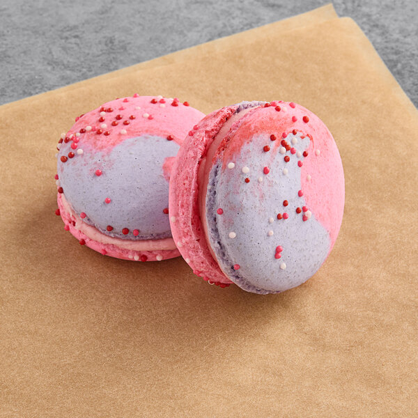Two Macaron Centrale raspberry caramel macarons on a piece of paper.