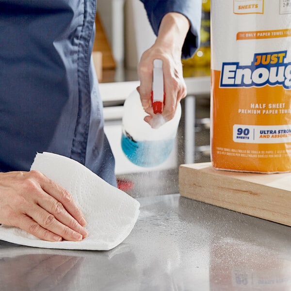 A person cleaning a counter in a professional kitchen using a Lavex Just Enough half sheet paper towel.